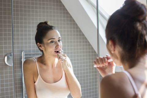 Midt-, kvinne pusse tennene i speilet på badet.